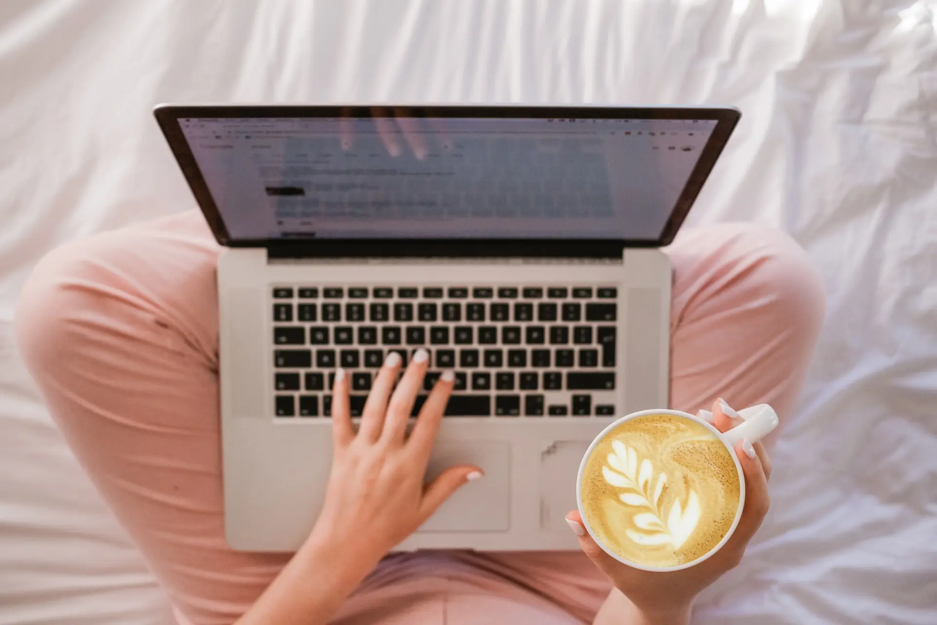 person using MacBook Pro and holding cappuccino
